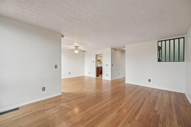 empty room featuring visible vents, a textured ceiling, light wood finished floors, baseboards, and ceiling fan