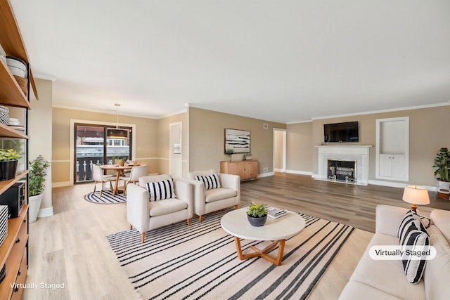 living area with a fireplace with flush hearth, baseboards, light wood-type flooring, and ornamental molding