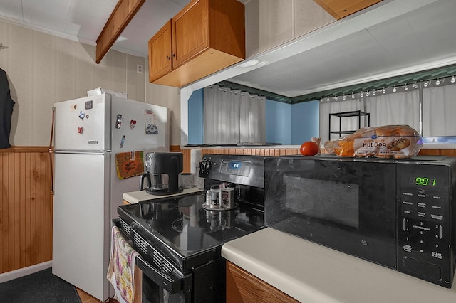 kitchen featuring black appliances, wooden walls, and brown cabinets