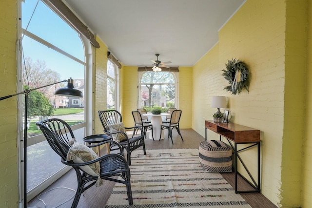 sunroom / solarium with brick wall, outdoor dining space, wood finished floors, and ceiling fan