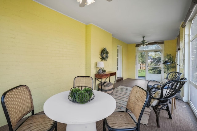 sunroom featuring brick wall, baseboards, and ceiling fan