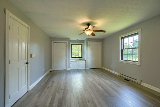 7704 Old Tarlton Pike, Circleville, OH 43113 - unfurnished bedroom featuring multiple closets, a baseboard radiator, multiple windows, wood finished floors, and a textured ceiling