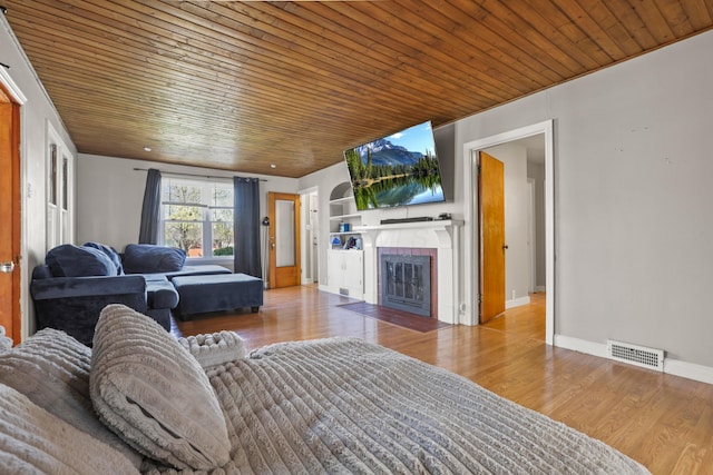 living area with a fireplace with flush hearth, visible vents, wood ceiling, wood finished floors, and baseboards