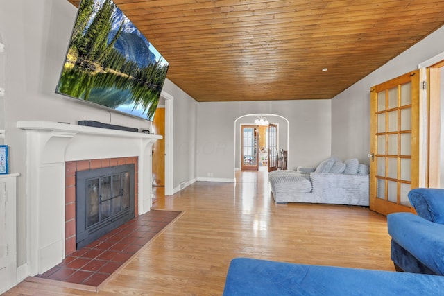 living area with arched walkways, an inviting chandelier, a tiled fireplace, wood ceiling, and wood finished floors