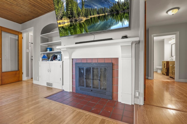 details with baseboards, built in features, a tiled fireplace, visible vents, and wood finished floors
