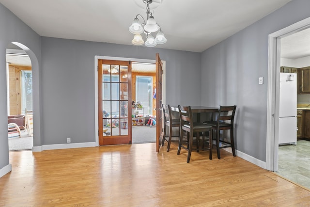 dining room with light wood finished floors, arched walkways, and a healthy amount of sunlight