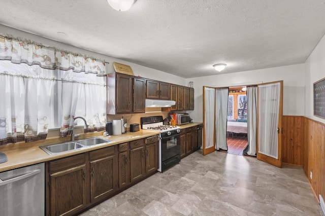 kitchen with appliances with stainless steel finishes, wood walls, a sink, wainscoting, and under cabinet range hood