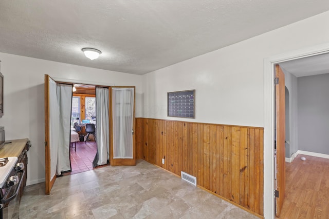 interior space featuring wooden walls, wainscoting, a textured ceiling, and visible vents