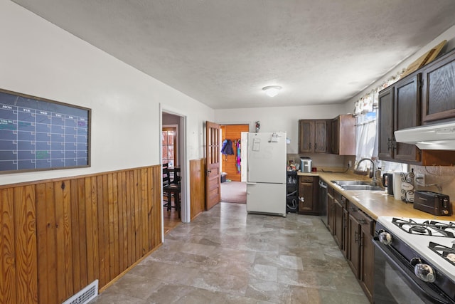 kitchen featuring a sink, light countertops, freestanding refrigerator, wood walls, and a wainscoted wall