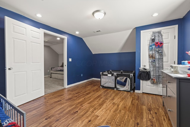 interior space featuring wood finished floors, baseboards, vaulted ceiling, and visible vents
