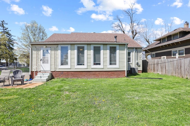 back of house featuring entry steps, a yard, fence, and roof with shingles