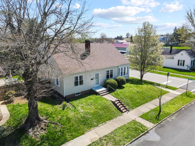 new england style home featuring a front yard, fence, a shingled roof, and a chimney
