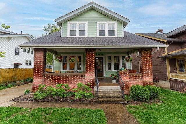 bungalow with roof with shingles, a porch, brick siding, and fence
