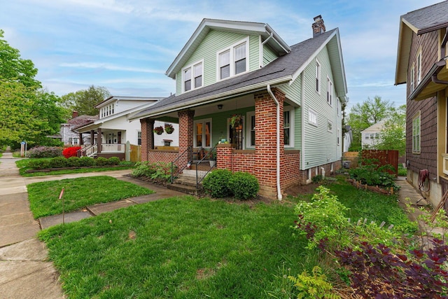bungalow-style house with a chimney, a porch, brick siding, and a front lawn