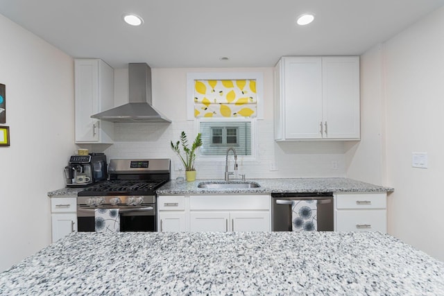 kitchen featuring light stone counters, a sink, backsplash, wall chimney range hood, and stainless steel appliances