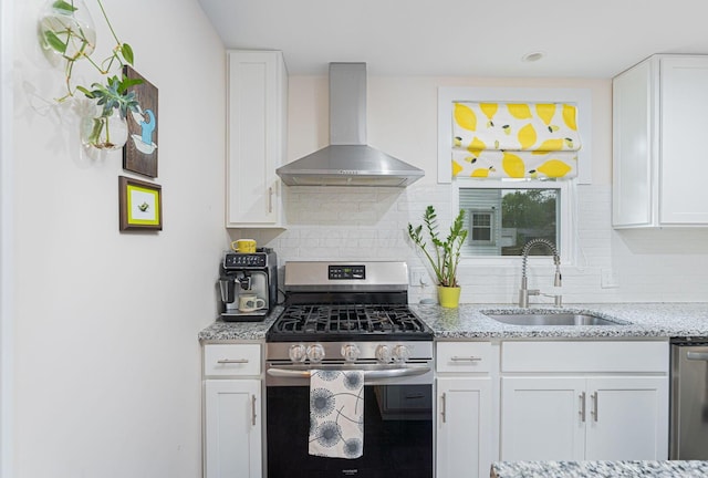 kitchen with a sink, stainless steel appliances, white cabinetry, and wall chimney range hood