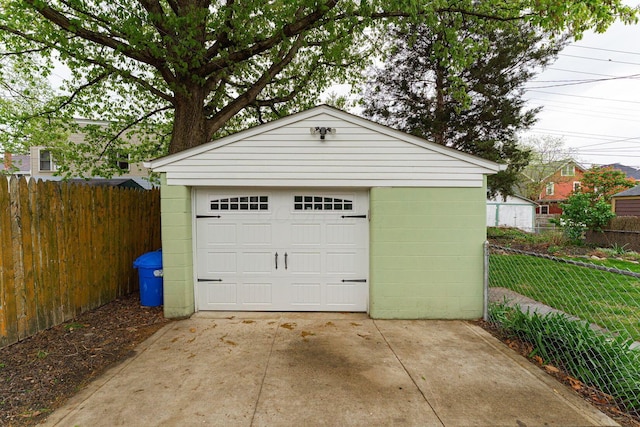 detached garage featuring concrete driveway and fence