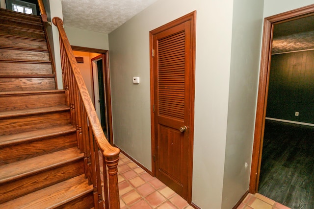 stairs with tile patterned flooring, baseboards, and a textured ceiling