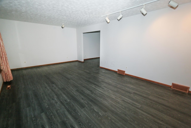 empty room featuring visible vents, dark wood-type flooring, a textured ceiling, and baseboards