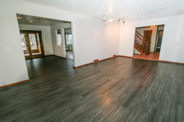 spare room featuring stairway, wood finished floors, baseboards, rail lighting, and a textured ceiling