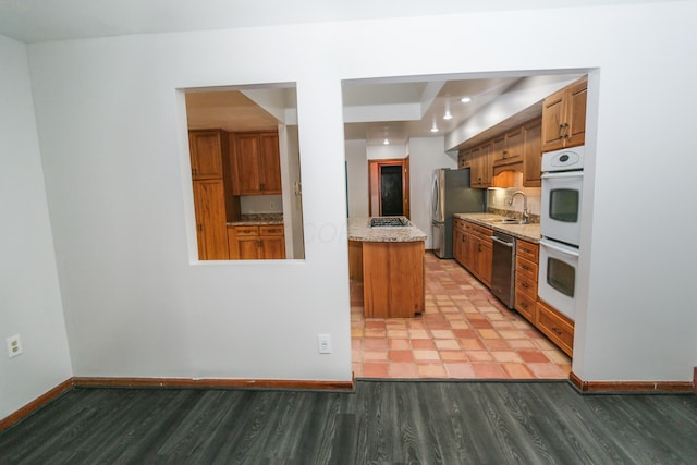 kitchen with light wood-type flooring, a sink, stainless steel appliances, brown cabinetry, and baseboards