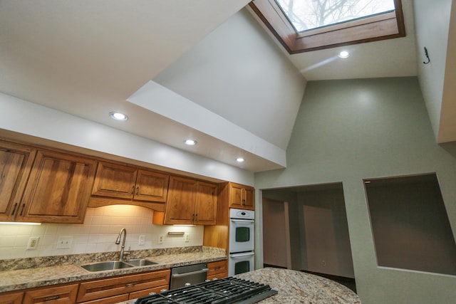 kitchen with a sink, a skylight, brown cabinetry, decorative backsplash, and dishwasher