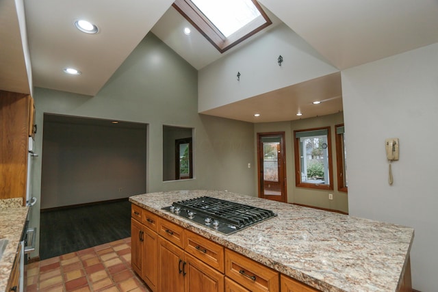 kitchen featuring light stone countertops, recessed lighting, a skylight, stainless steel gas stovetop, and brown cabinetry