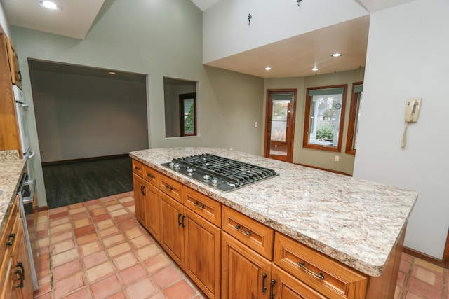 kitchen featuring a center island, recessed lighting, stainless steel gas stovetop, brown cabinetry, and baseboards