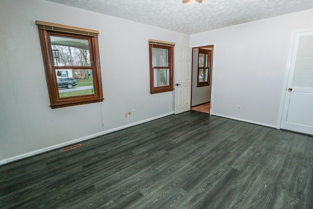 unfurnished room with visible vents, a textured ceiling, dark wood-type flooring, and baseboards