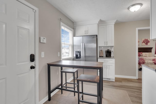 1333 Carolyn Ave, Columbus, OH 43224 - kitchen with stainless steel fridge with ice dispenser, light wood-style flooring, a textured ceiling, white cabinetry, and decorative backsplash