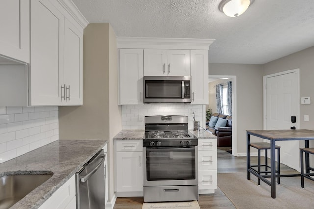 1333 Carolyn Ave, Columbus, OH 43224 - kitchen featuring white cabinets, wood finished floors, light stone countertops, decorative backsplash, and stainless steel appliances