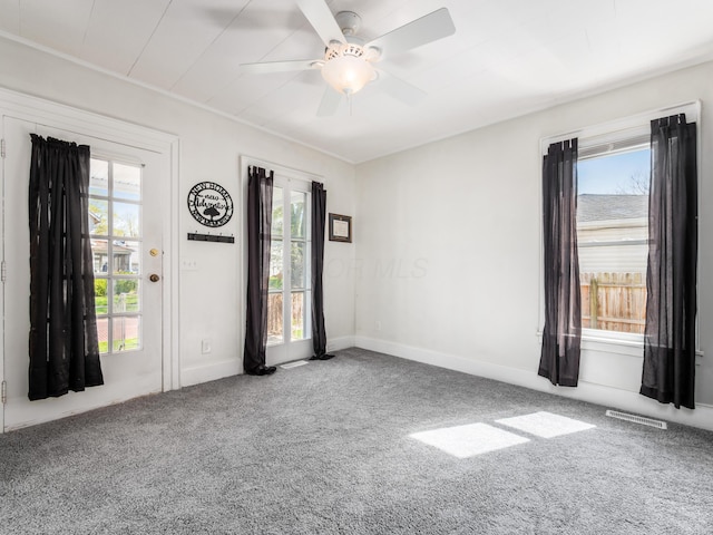 carpeted spare room with a ceiling fan, visible vents, baseboards, and a healthy amount of sunlight