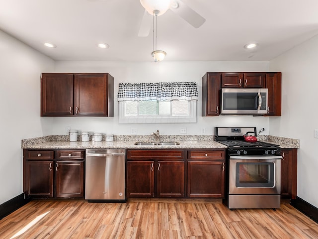 kitchen featuring a sink, appliances with stainless steel finishes, ceiling fan, light wood-type flooring, and light stone countertops