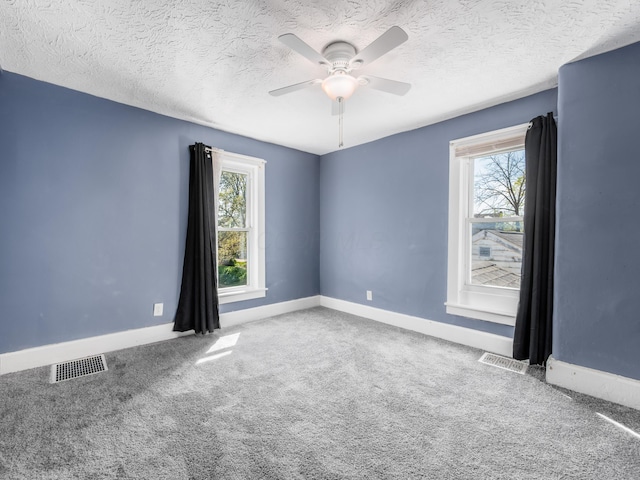 carpeted spare room with a healthy amount of sunlight, visible vents, and baseboards