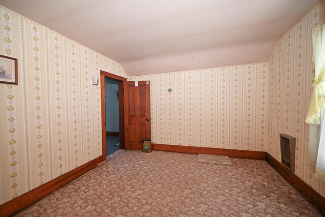 unfurnished room featuring wallpapered walls, baseboards, carpet, lofted ceiling, and heating unit