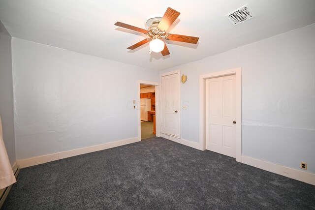 unfurnished bedroom featuring visible vents, baseboards, dark carpet, freestanding refrigerator, and a ceiling fan