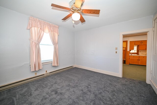 empty room with a wealth of natural light, a ceiling fan, baseboard heating, and carpet floors