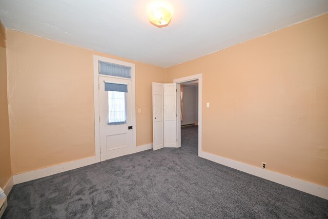unfurnished room with a baseboard radiator, baseboards, and dark carpet