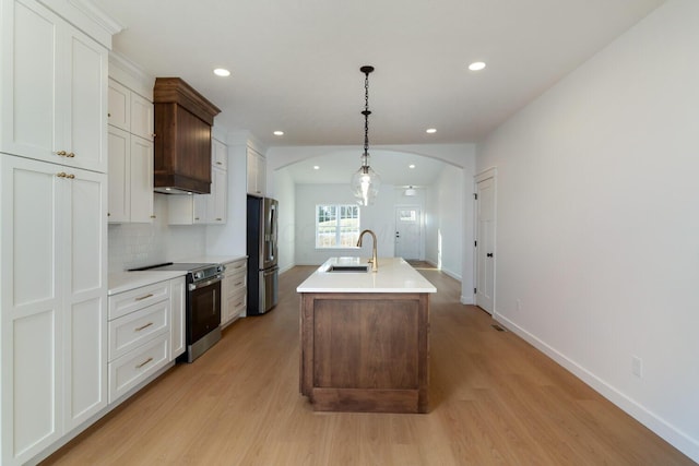 kitchen with light wood finished floors, a sink, arched walkways, stainless steel appliances, and a kitchen island with sink
