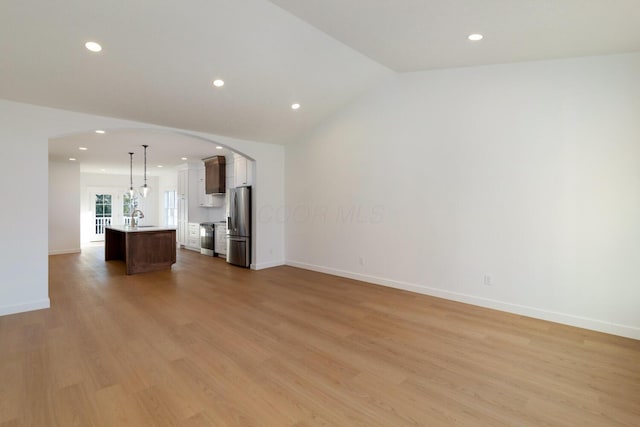 unfurnished living room with light wood finished floors, baseboards, vaulted ceiling, arched walkways, and a sink