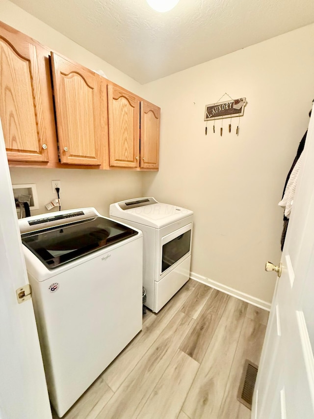 laundry room featuring cabinet space, light wood finished floors, baseboards, visible vents, and washer and clothes dryer