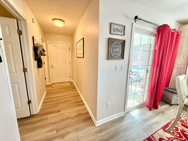 doorway to outside with a textured ceiling, baseboards, and light wood-type flooring