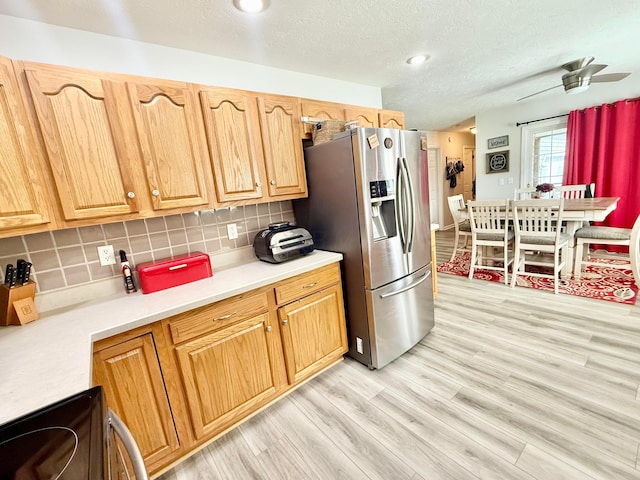 kitchen featuring light countertops, backsplash, stainless steel fridge, and light wood-style flooring