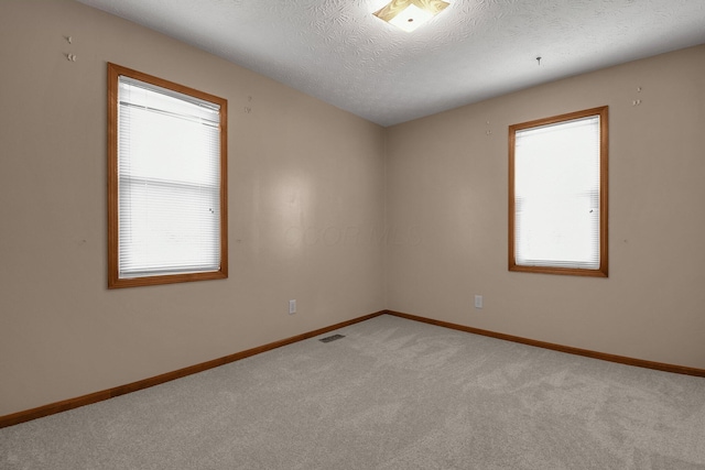 spare room featuring light carpet, a textured ceiling, baseboards, and visible vents