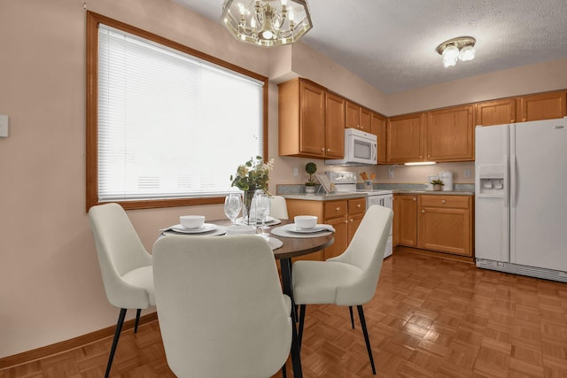 kitchen with a textured ceiling, baseboards, white appliances, an inviting chandelier, and light countertops