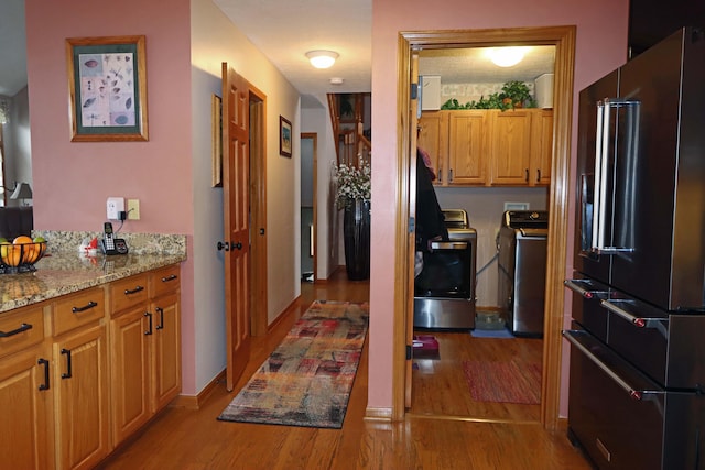 kitchen with light wood finished floors, baseboards, washer and clothes dryer, high end black refrigerator, and light stone counters
