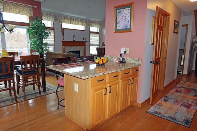 kitchen with baseboards, a kitchen bar, light wood-type flooring, light stone counters, and a tile fireplace