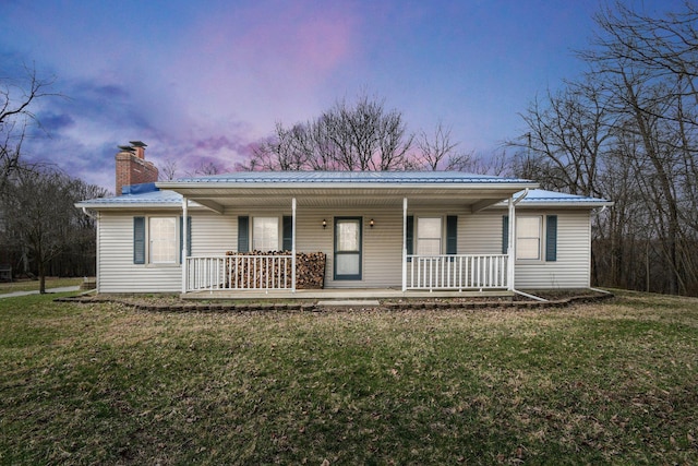 ranch-style home with a chimney, metal roof, a porch, and a front yard