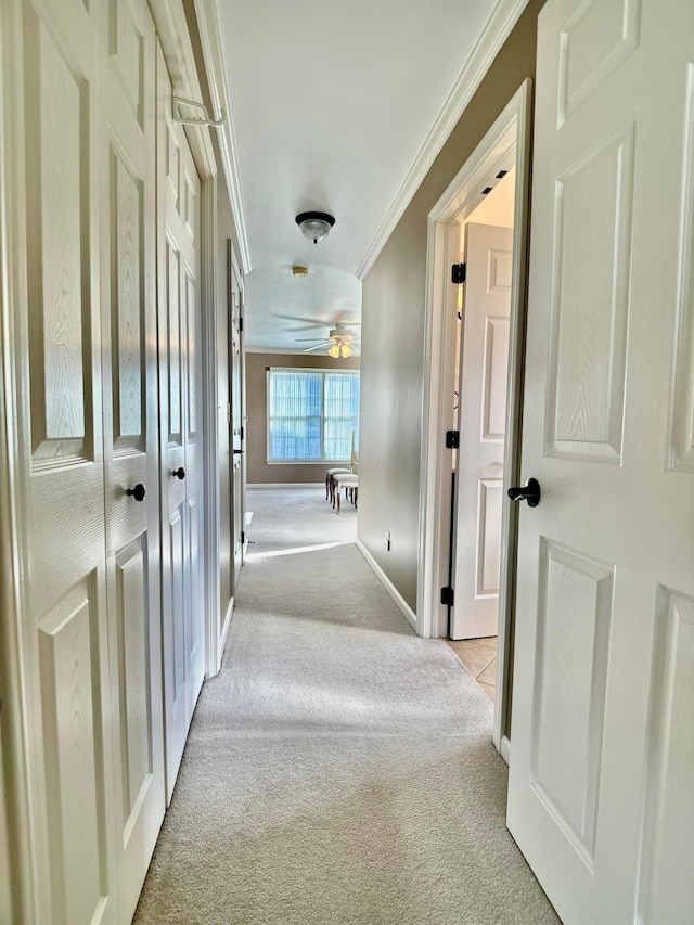 corridor with baseboards, light colored carpet, and ornamental molding