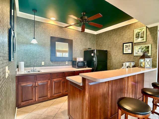 kitchen with a sink, stainless steel microwave, freestanding refrigerator, a breakfast bar area, and light countertops